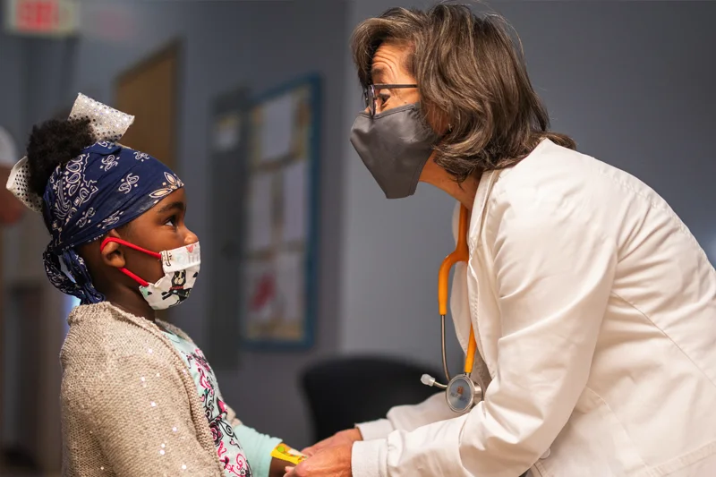 A young girl is being examined by a nurse wearing a mask.