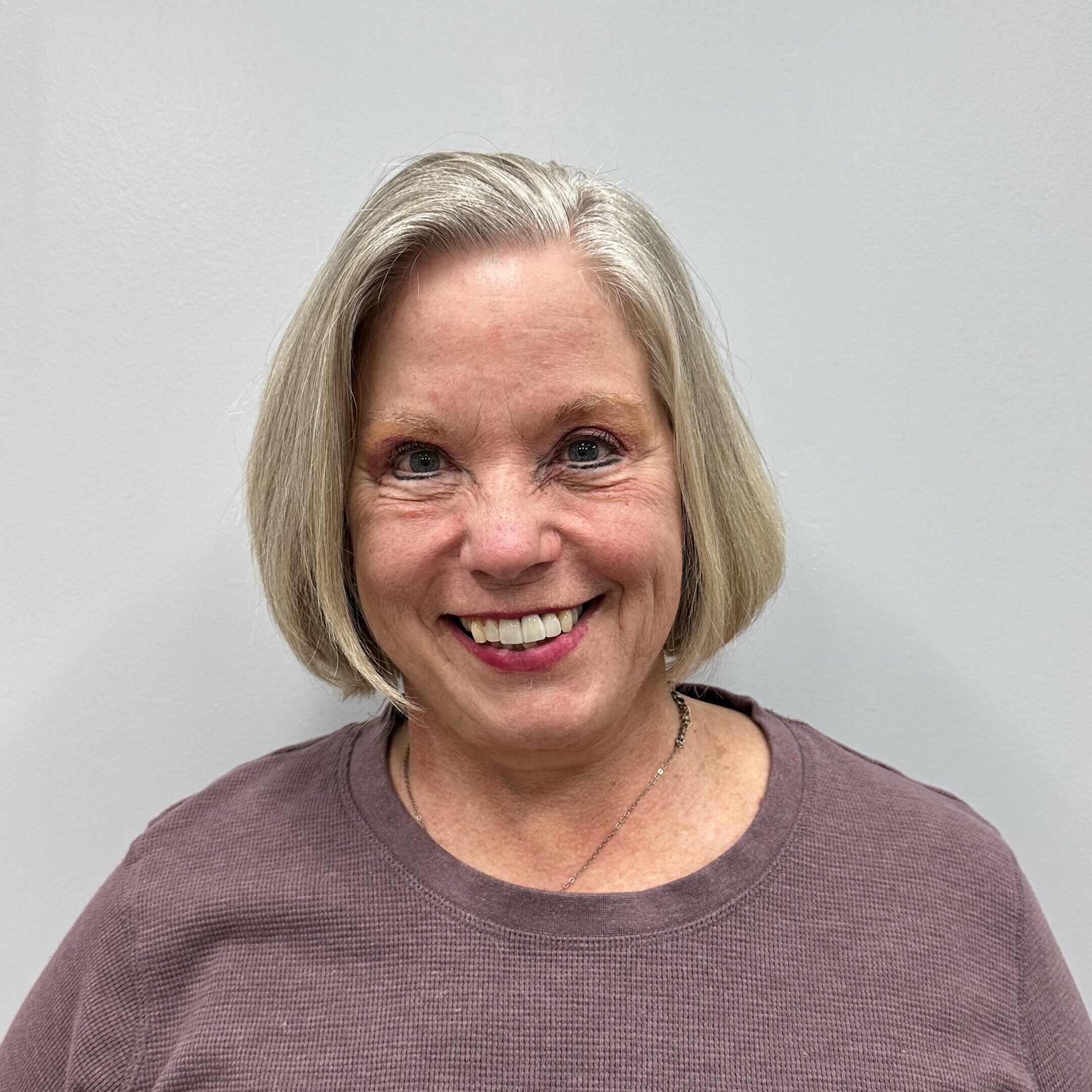 Headshot of D'Nice Cardin wearing a brown top against a white wall