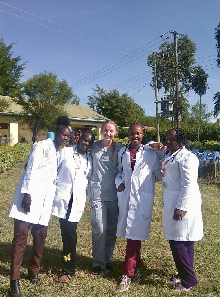 A nursing student in scrubs is joined by four nurses from Kenya in white coats. 