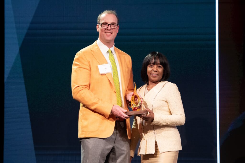 A woman receives a small award shaped like a flame from a man on stage. They are both smiling at the camera.