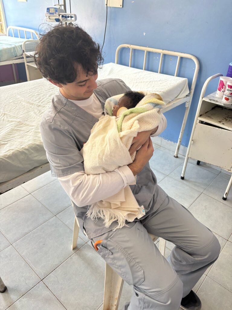 A male is seen holding a baby and smiling looking at it.