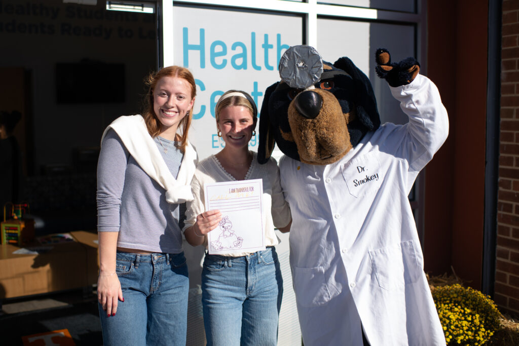 Two students pose with Smokey mascot outside of Vine School Health Center