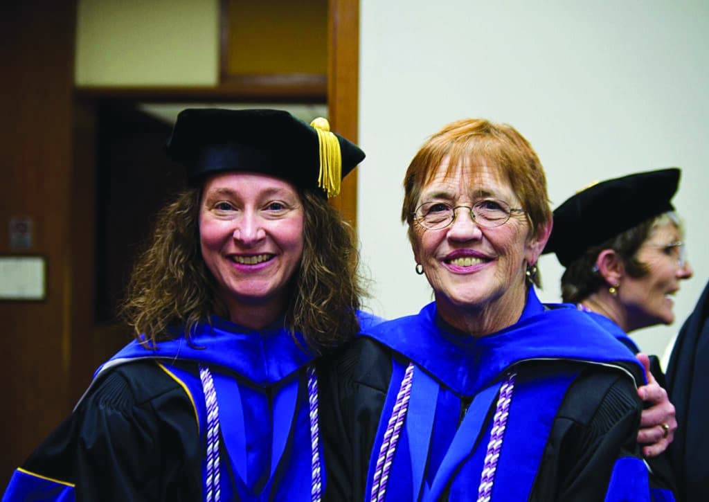 Two women in regalia pose smiling for a photo.