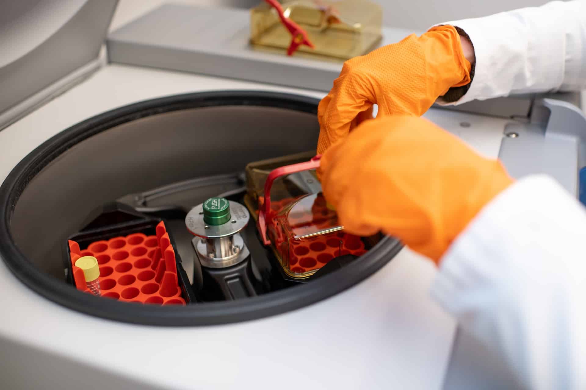 An individual in orange gloves working on lab equiptment